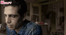 a man in a plaid shirt is sitting at a table in a room .