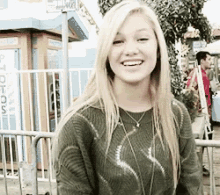 a blonde woman wearing a green sweater is smiling in front of a booth that says photos