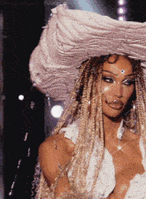a woman with braids is wearing a white top and a large hat
