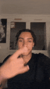 a young man in a black shirt is making a funny face with his finger in his mouth .