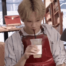 a man in an apron is drinking from a cup with a straw .