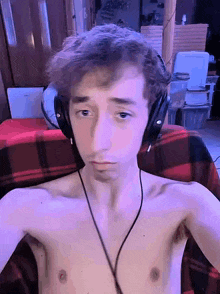a shirtless young man wearing headphones is sitting on a plaid blanket .