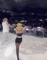 a woman in a black top and shorts is dancing on a stage in front of a crowd