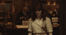 a woman in a white shirt is standing in a dark room waving her hand .