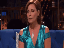 a woman is sitting on a blue couch wearing a blue dress and necklace