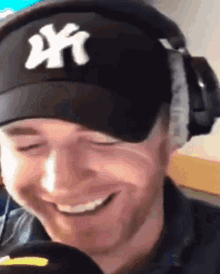 a man wearing a ny hat and headphones is smiling and looking at the camera .