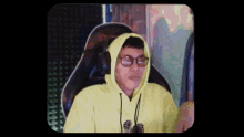 a man wearing glasses and a yellow hoodie is sitting in a chair