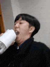 a young man is drinking from a white cup with his mouth open
