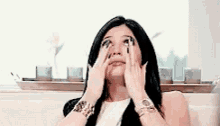 a woman is covering her eyes with her hands while looking up .