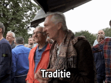two older men are standing in a crowd and one of them is wearing an orange jacket that says traditione on it