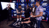 a group of men are standing around a man in a wheelchair in front of a sign that says aew dynamite .