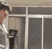 a woman in a striped shirt is standing in a room with a sliding glass door .