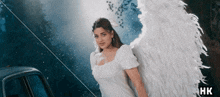 a woman in a white dress with angel wings stands in front of a car