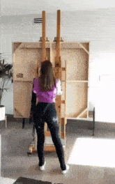 a woman in a purple shirt is standing in front of a wooden easel .