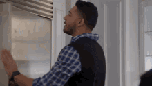 a man in a plaid shirt is opening a stainless steel refrigerator door .