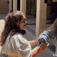 a woman wearing glasses holds another woman 's arm in a hallway