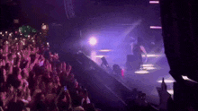 a crowd of people watching a concert with purple lights behind them
