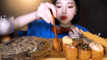 a woman in a blue shirt is eating noodles and sushi
