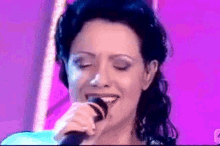 a close up of a woman singing into a microphone with her eyes closed
