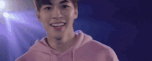 a young man wearing a pink hoodie is standing in front of a purple background .