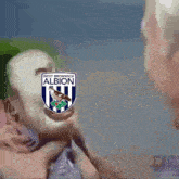 a man holding another man 's head with a west bromwich albion logo on it