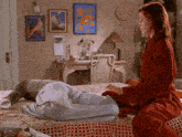 a woman in a red robe sits on a bed next to a man
