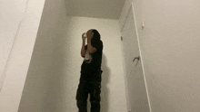 a man in a black shirt and black pants is standing in a hallway next to a white door .