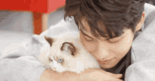 a young man is laying on the floor with a white cat on his chest .