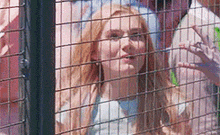 a woman with red hair is behind a fence .