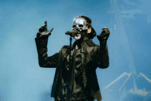 a man wearing a skull mask and gloves stands in front of a microphone