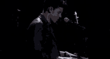 a young man is playing a piano and singing into a microphone in a dark room .