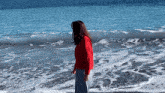 a woman in a red sweater stands on a beach near the ocean