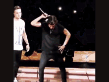 a man in a black shirt is dancing on a stage while another man stands behind him .
