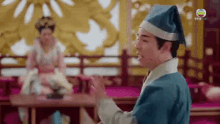 a man in a blue robe and hat is standing in front of a woman in a costume .
