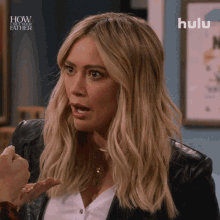 a woman in a black leather jacket is talking to another woman in front of a sign that says how i met your father
