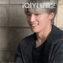 a young man with gray hair is smiling and wearing a black jacket and a black shirt .