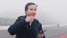 a man wearing a black jacket is standing on a foggy road with think jules written on the bottom right