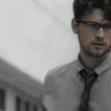 a man wearing glasses and a tie is walking down stairs .