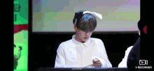 a young boy wearing a white shirt and bunny ears is sitting at a desk .