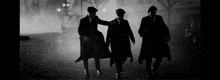 three men in suits and hats are walking down a street at night
