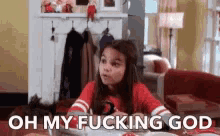 a little girl is sitting at a table with the words `` oh my fucking god '' written on her face .