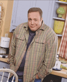 a man wearing a plaid shirt is standing in a kitchen