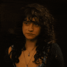 a woman with curly hair is wearing a necklace with a pendant