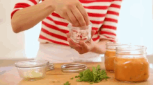 a woman in a red and white striped shirt is preparing food in jars .