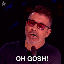 a man wearing sunglasses and a black shirt says oh gosh in front of a microphone