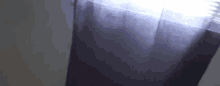 a purple curtain is hanging on a window with a light shining through it .