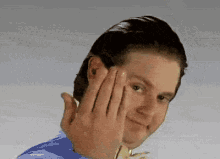 a man in a blue shirt is covering his face with his hands