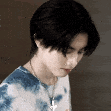 a young man wearing a tie dye shirt and a necklace with a cross pendant .