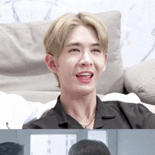 a young man with blonde hair is sitting on a couch smiling