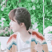a woman wearing a colorful sweater is holding chopsticks in her hand